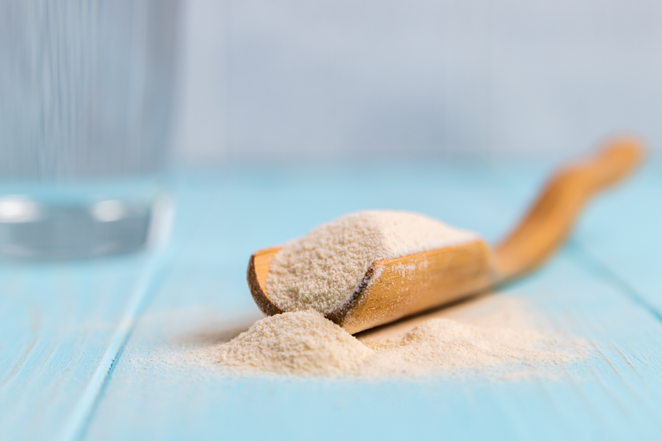Closeup of a serving of psyllium powder on a wooden spoon with a glass of water in the background